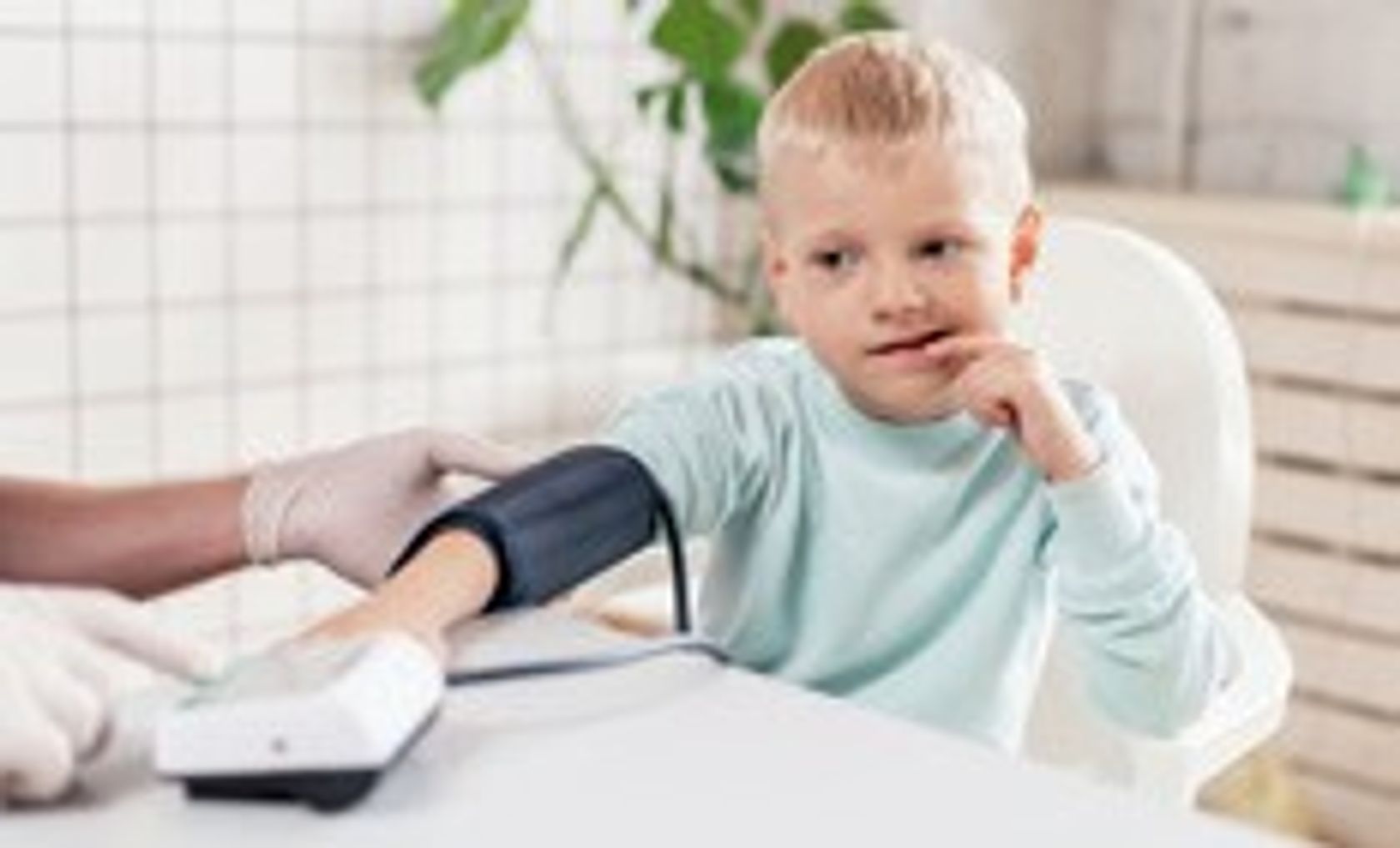 Kind mit angelegter Blutdruckmess-Manschette sitzt am Tisch.