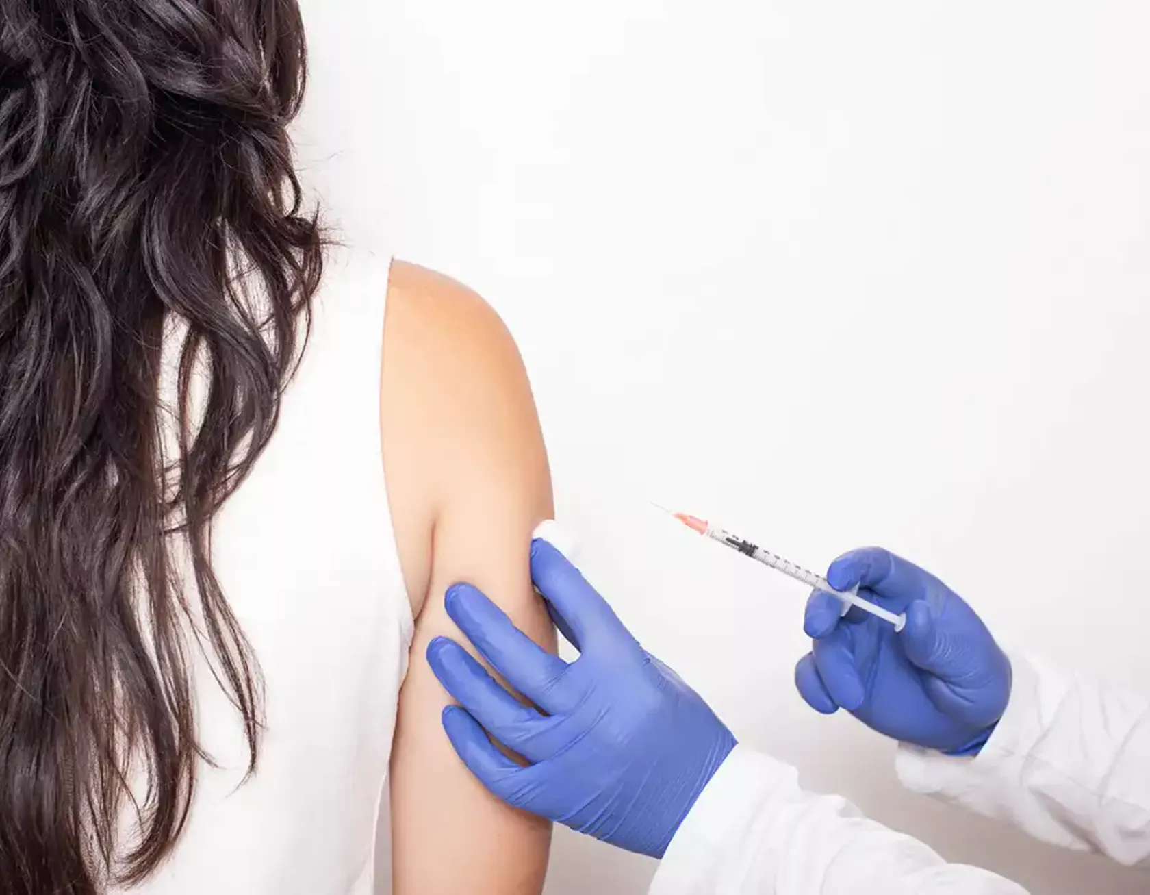 Eine Frau erhält eine Impfung in den rechten Oberarm, von hinten gesehen.