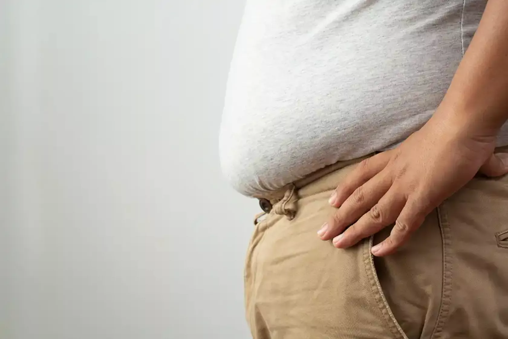 Blick auf den Bauch eines übergewichtigen Mannes, der über den Hosenbund hängt.