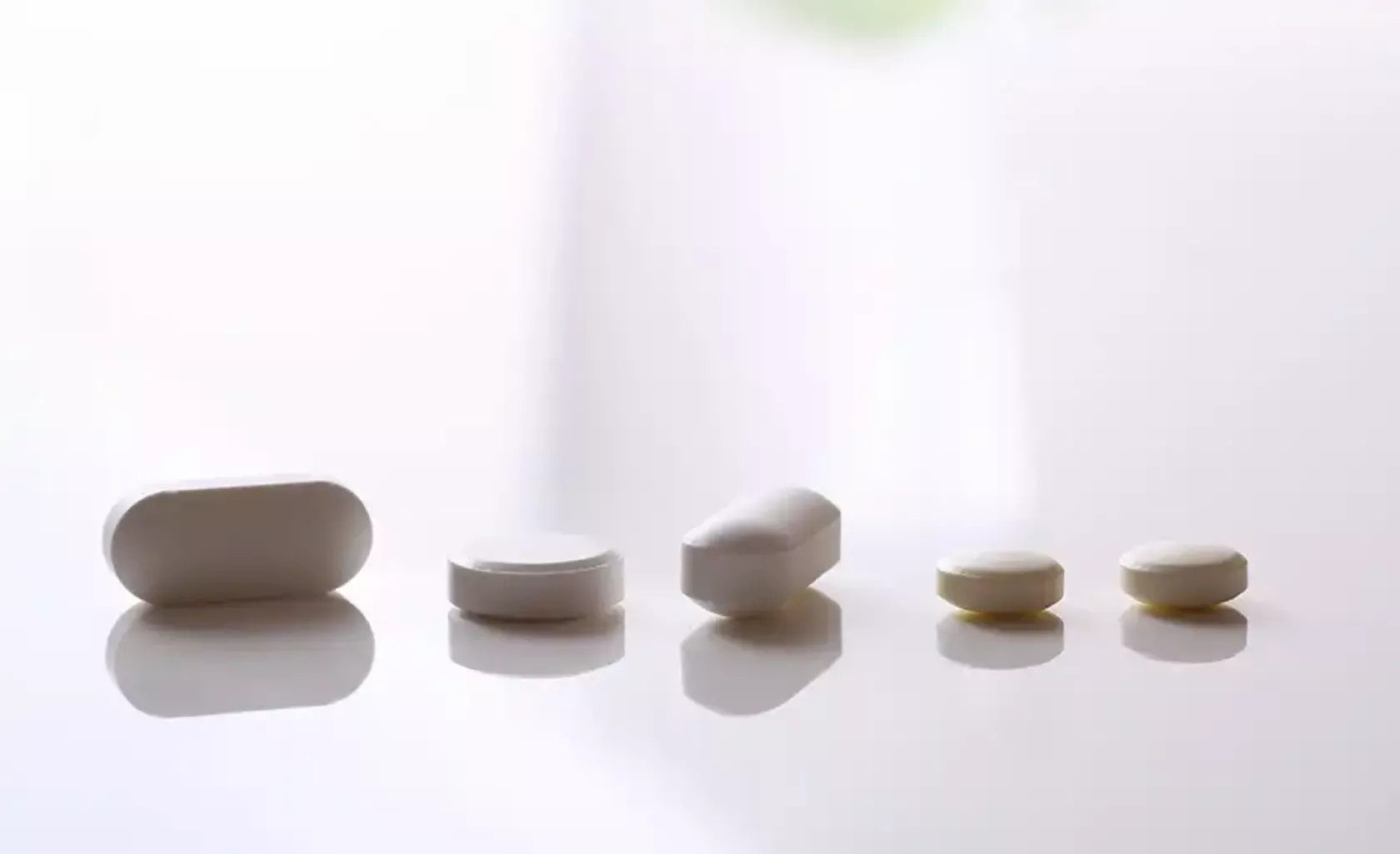 Weiße Kapseln und Tabletten auf einem glänzenden weißen Tisch.