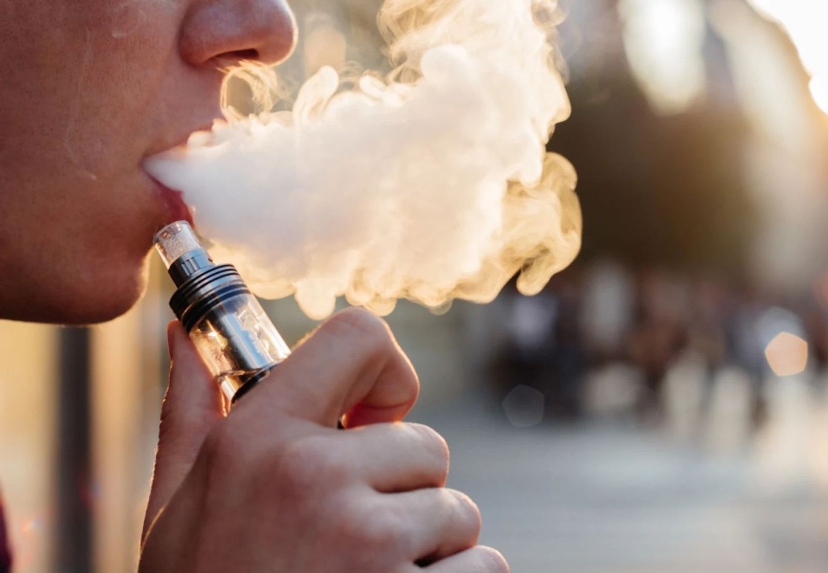 Vaping - ein junger Mann bläst eine dicke Wolke Dampf aus einer E-Zigarette aus.