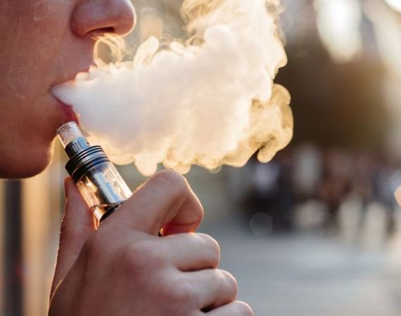 Vaping - ein junger Mann bläst eine dicke Wolke Dampf aus einer E-Zigarette aus.