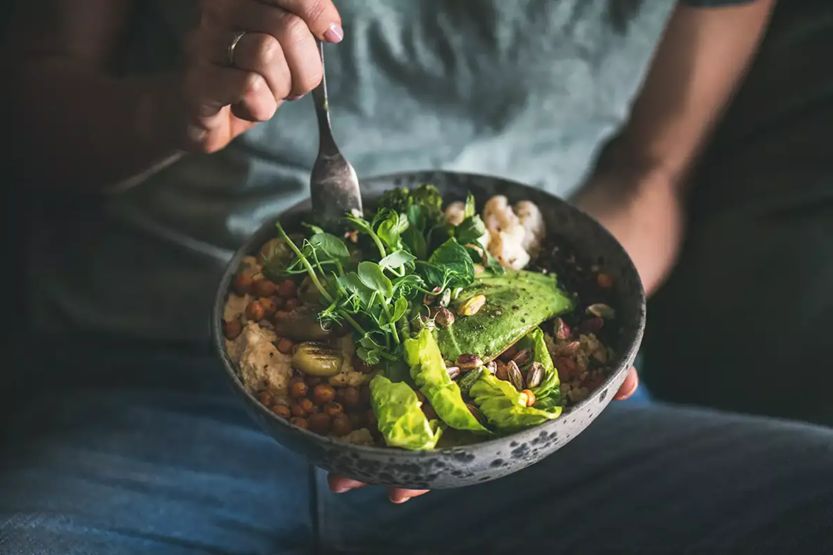 Eine Bowl mit veganem Gericht mit Avocado hält ein Mann auf dem Schoßl