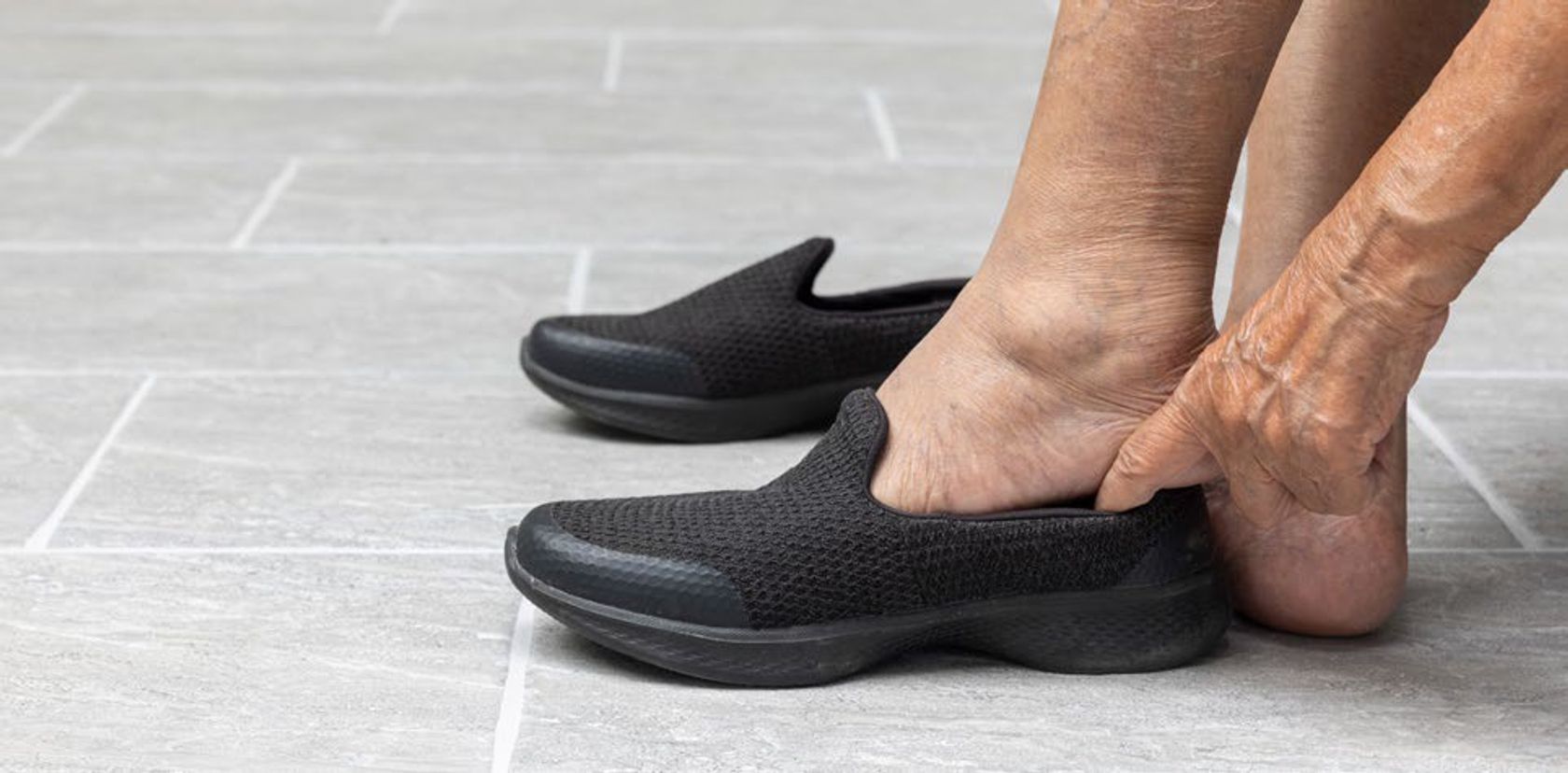Man sieht die nackten Füße einer älteren Person, die sich mit Mühe Schuhe anzieht.